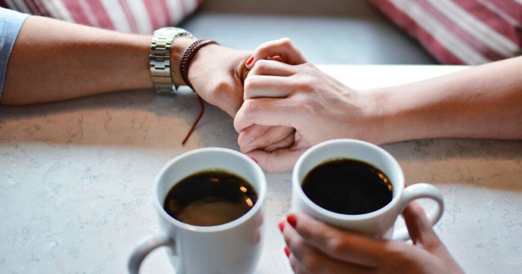 コーヒーを飲みながら落ち着いた感じで手を握り合うカップル
