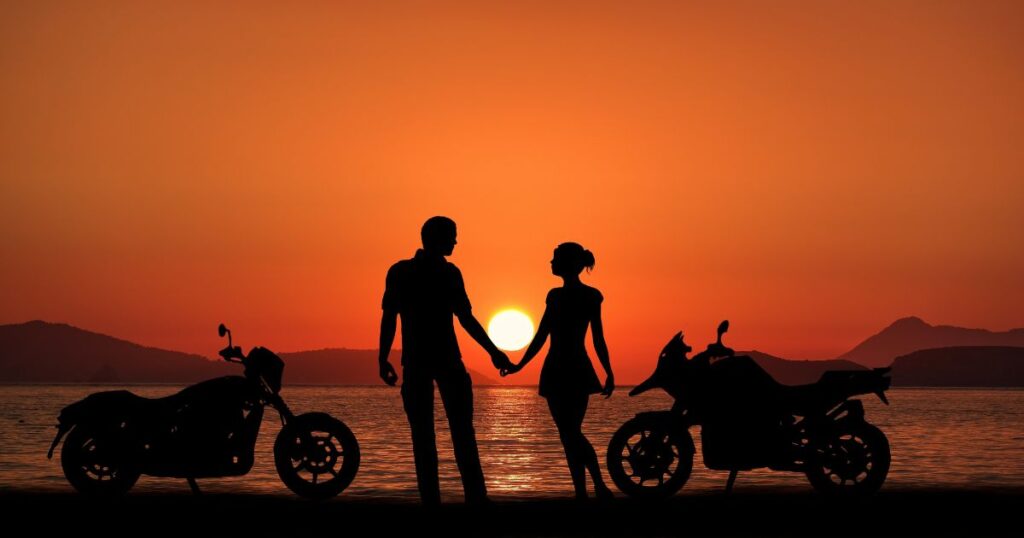 夕焼けに照らされるバイクで海辺まで来たカップル