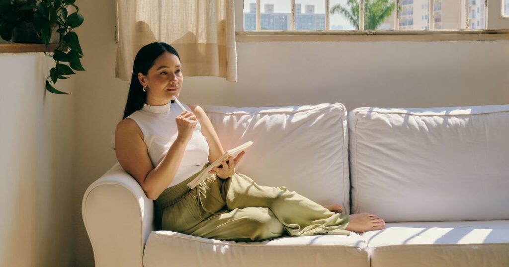 ソファに腰を下ろし考えたことをメモする女性
