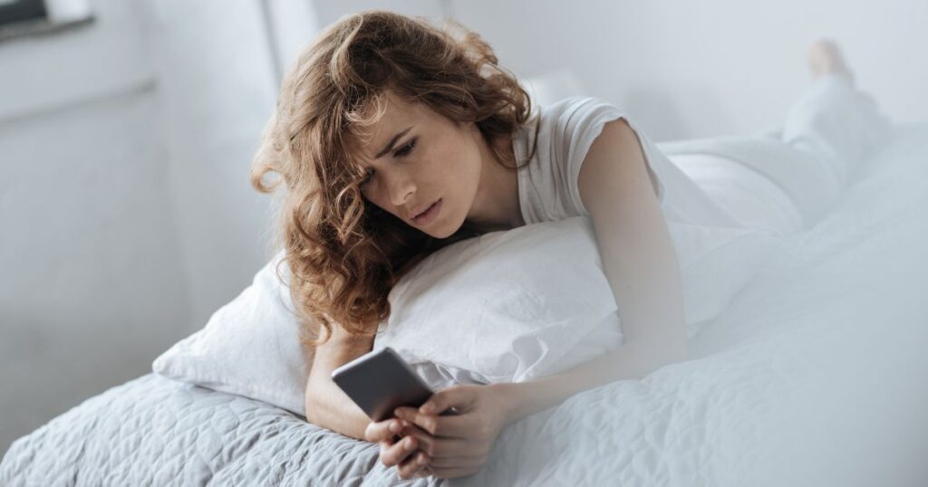 ベッドに寝そべりスマホをチェックする女性