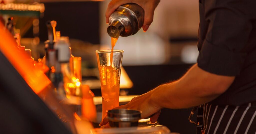シェイカーからグラスへお酒を注ぐバーテンダーの男性