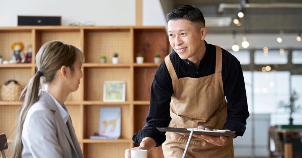 女性に飲み物を差し出すカフェの男性店員