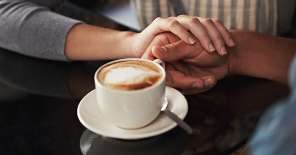 コーヒーカップを持つ男性の手を握る女性