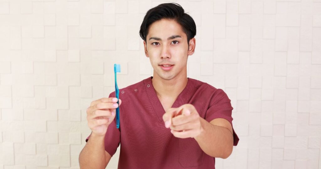 歯ブラシを持ってこちらを指差す歯科衛生士の男性