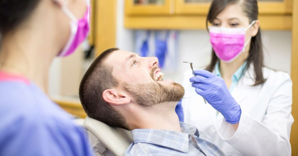 口を開けて歯科衛生士の女性に治療してもらう男性