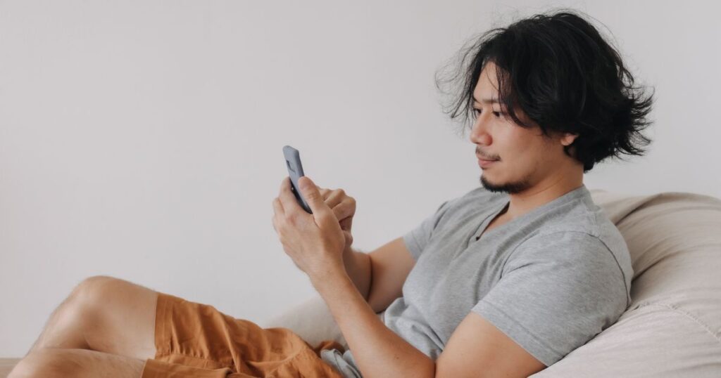 椅子に腰を下ろしてスマホをいじる男性