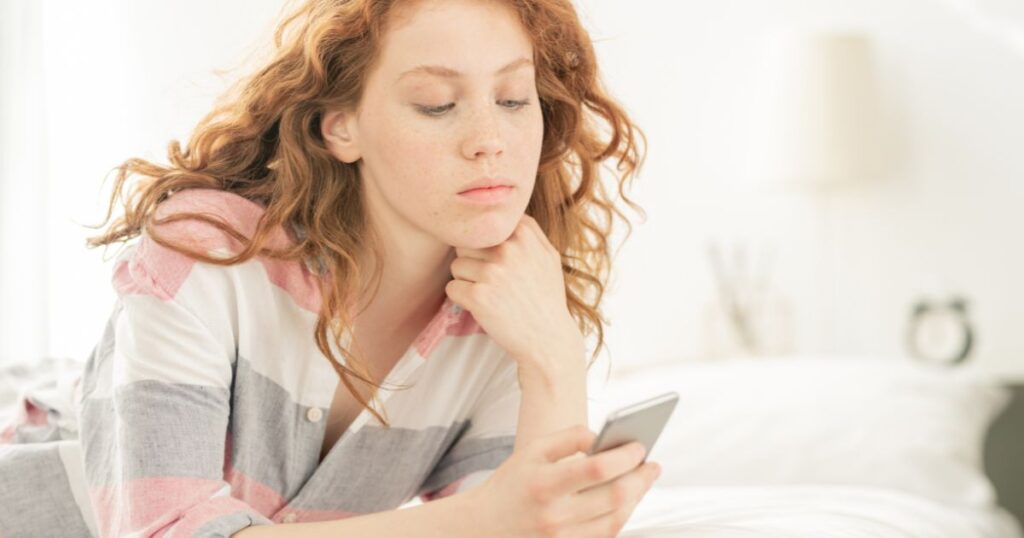 ベッドに寝そべりスマートフォンの通知をチェックする女性