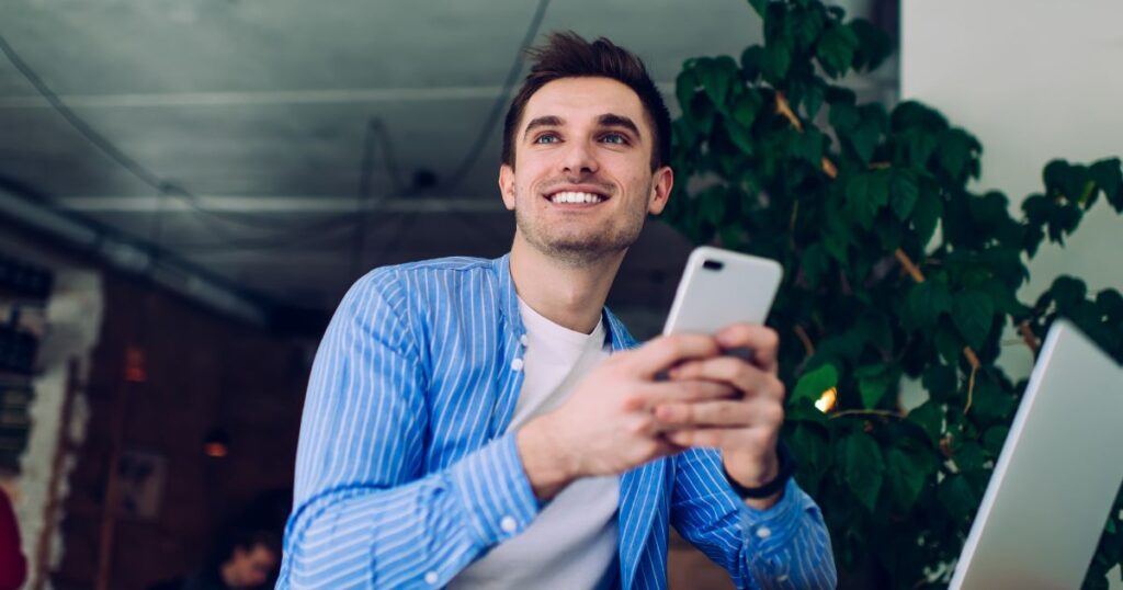 スマホを操作しながら微笑む青いシャツの男性