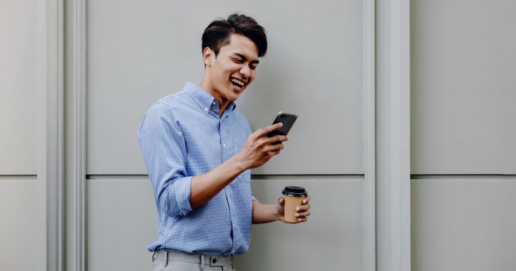 スマホを見て笑う青いシャツの男性