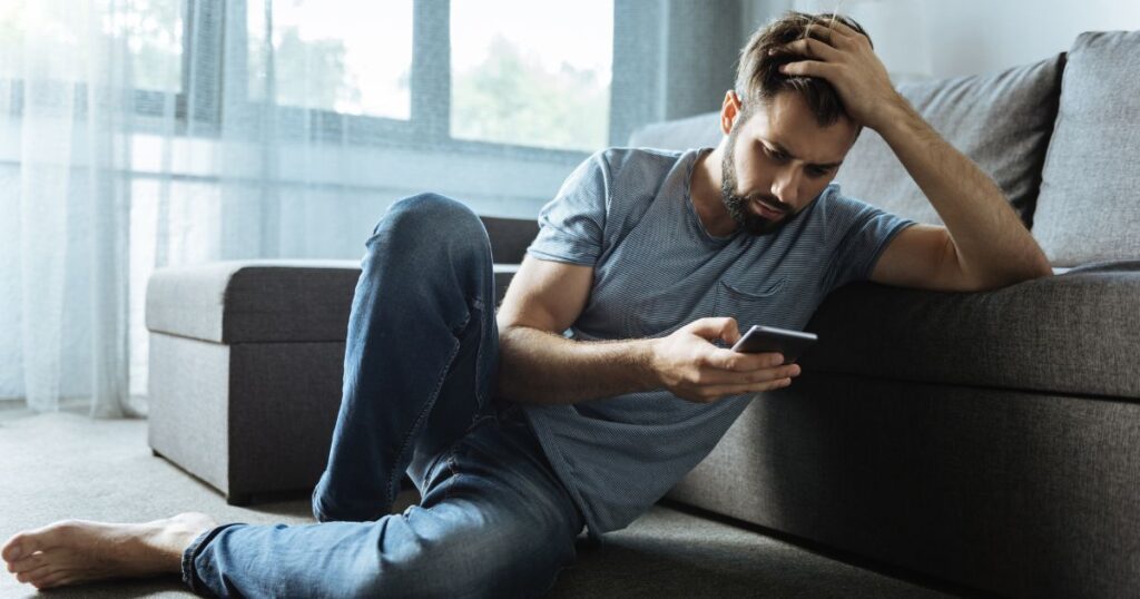 スマホをの画面を見て頭を抱える男性