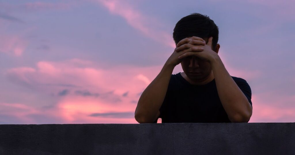 夕暮れの中、頭を抱えて後悔する男性