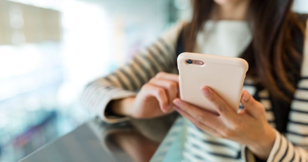 ピンクのスマホを操作するゼブラ柄のロンTを着た女性